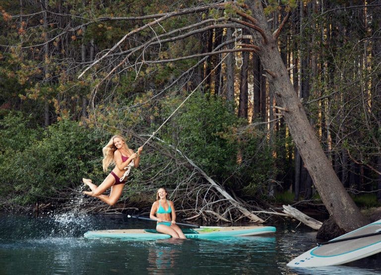 Two young women enjoying a rope swing on a small mountain lake.