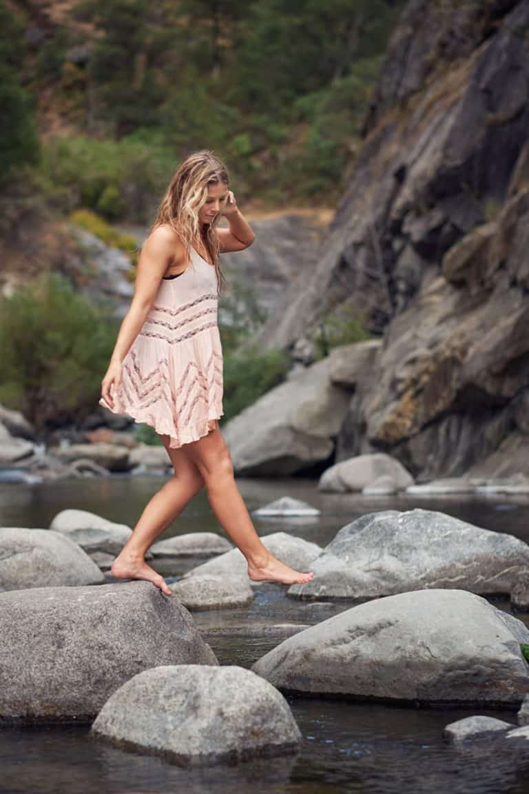 A Barefoot Woman in a Dress Walking Across a Creek.