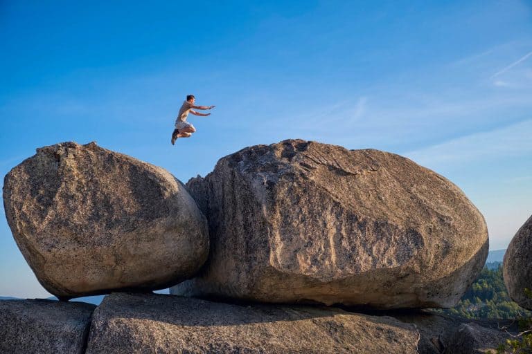 Teenage boy in a remote location in Northern California jumping from one large boulder to another one.