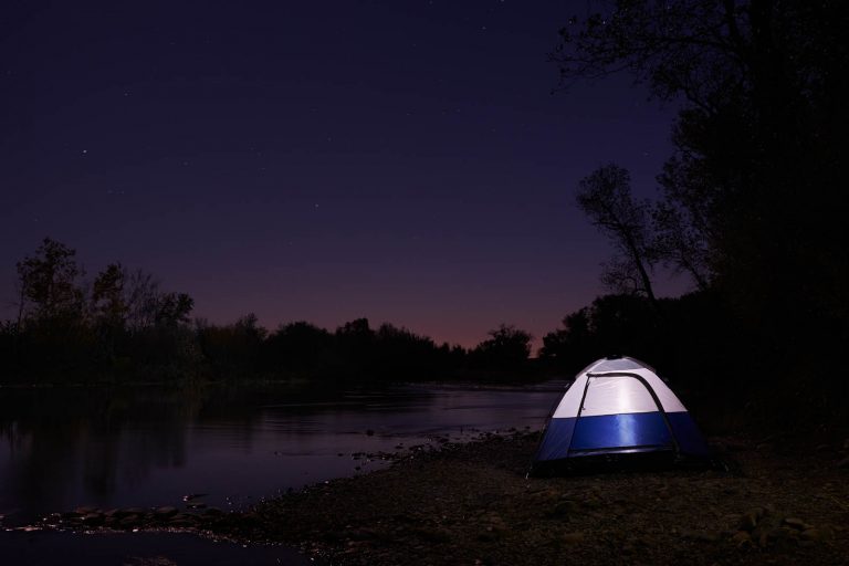 An illuminated tent on the edge of the Feather River in Northern California at night