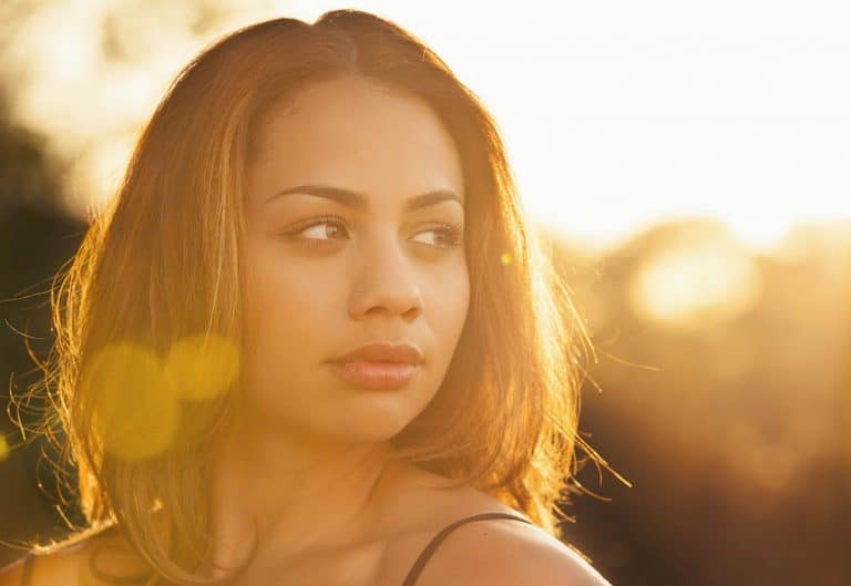 Backlit portrait with lens flare of a young woman staring into the distance on a summer day.