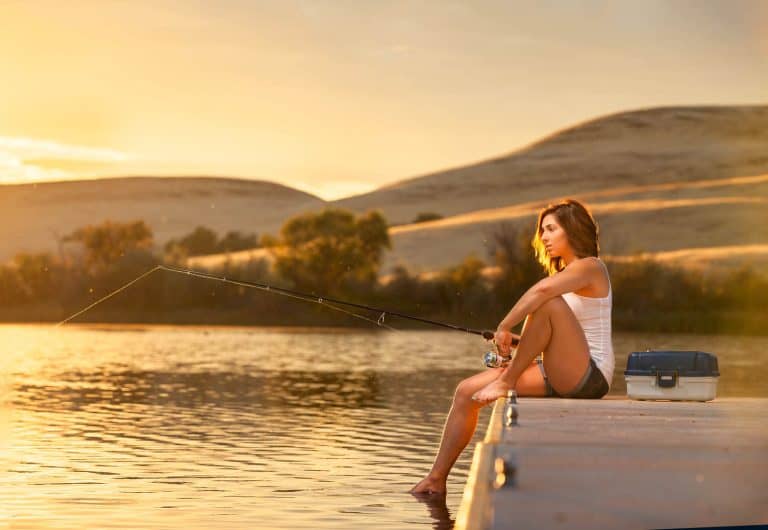 Young woman fishing from a dock on a small lake at sunset.