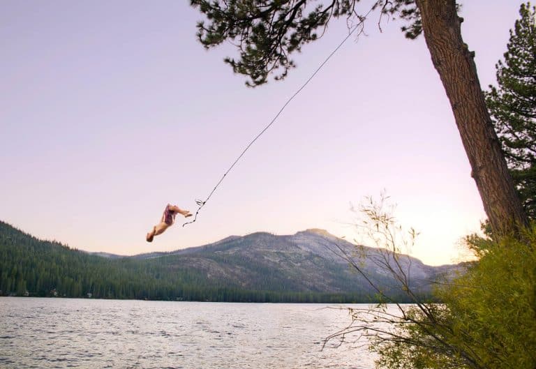 A you man doing a backflip off a rope swing.