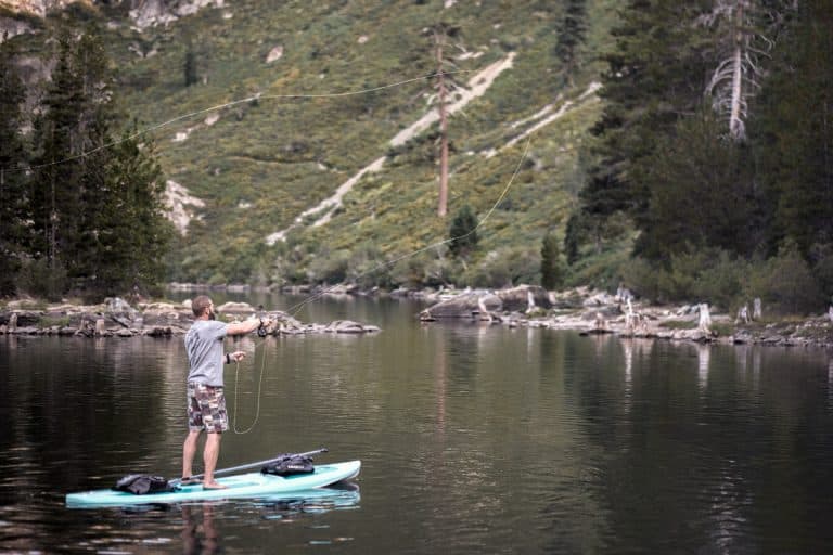 A man casting a fly pole while standing on a paddle board in a mountain lake in Northern California,