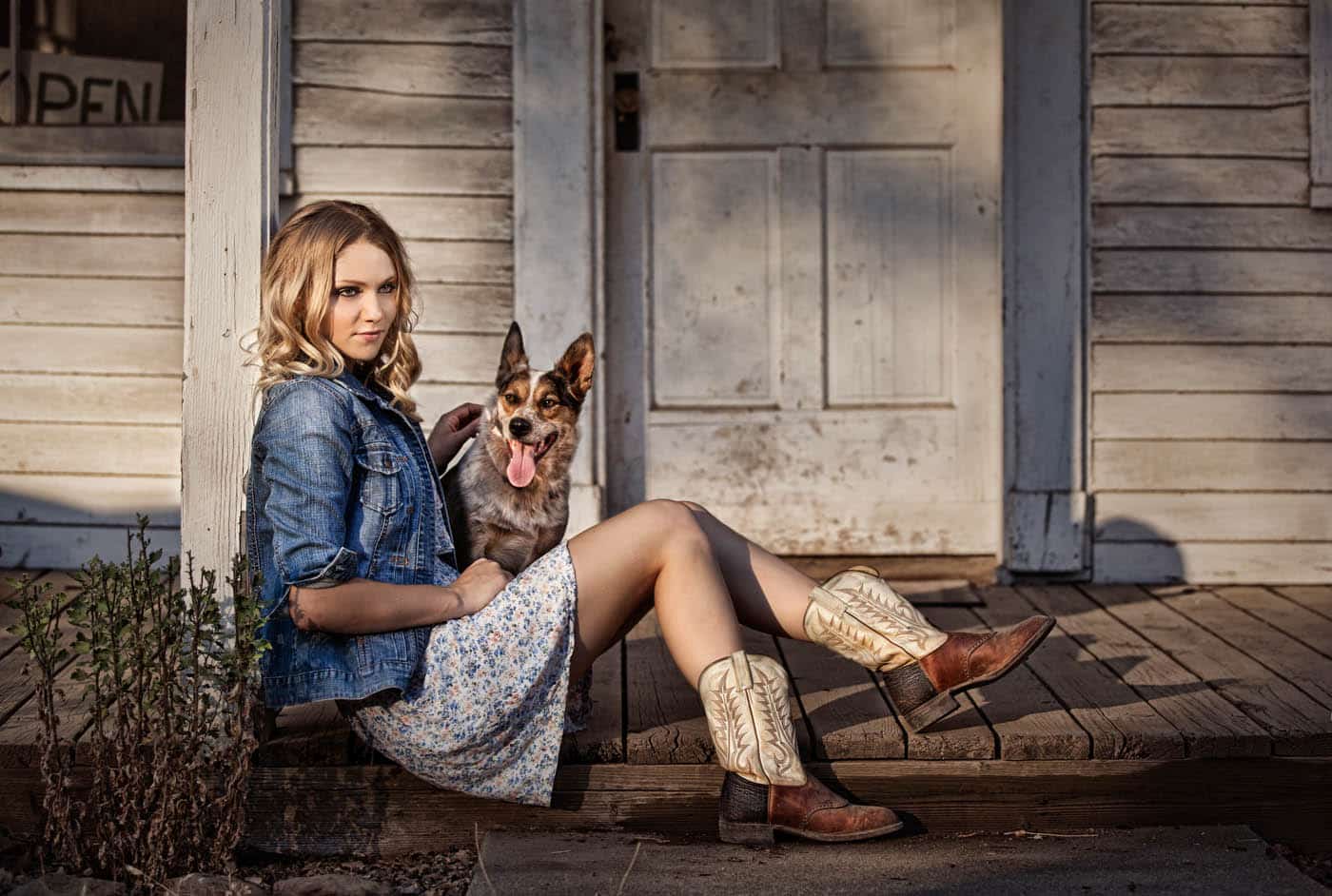 Country Girl in cowboy boots sitting on a front porch with her dog.
